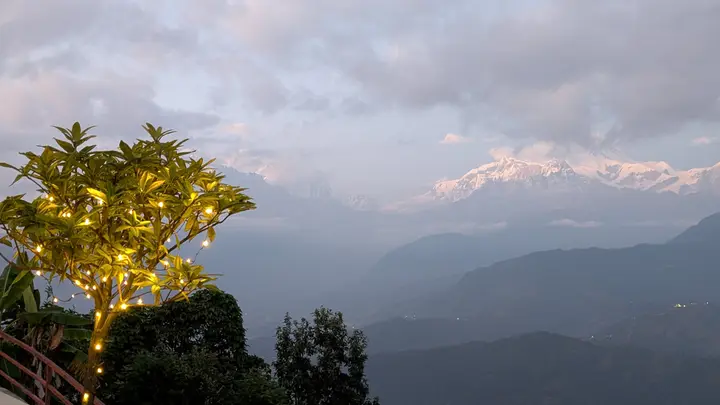A small tree strung with warm fairy lights in front of the snow-covered Annapurna range at dusk