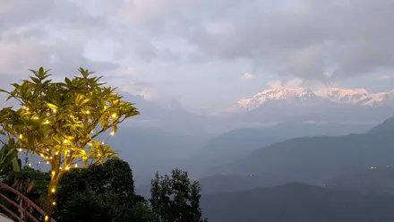 A small tree strung with warm fairy lights in front of the snow-covered Annapurna range at dusk