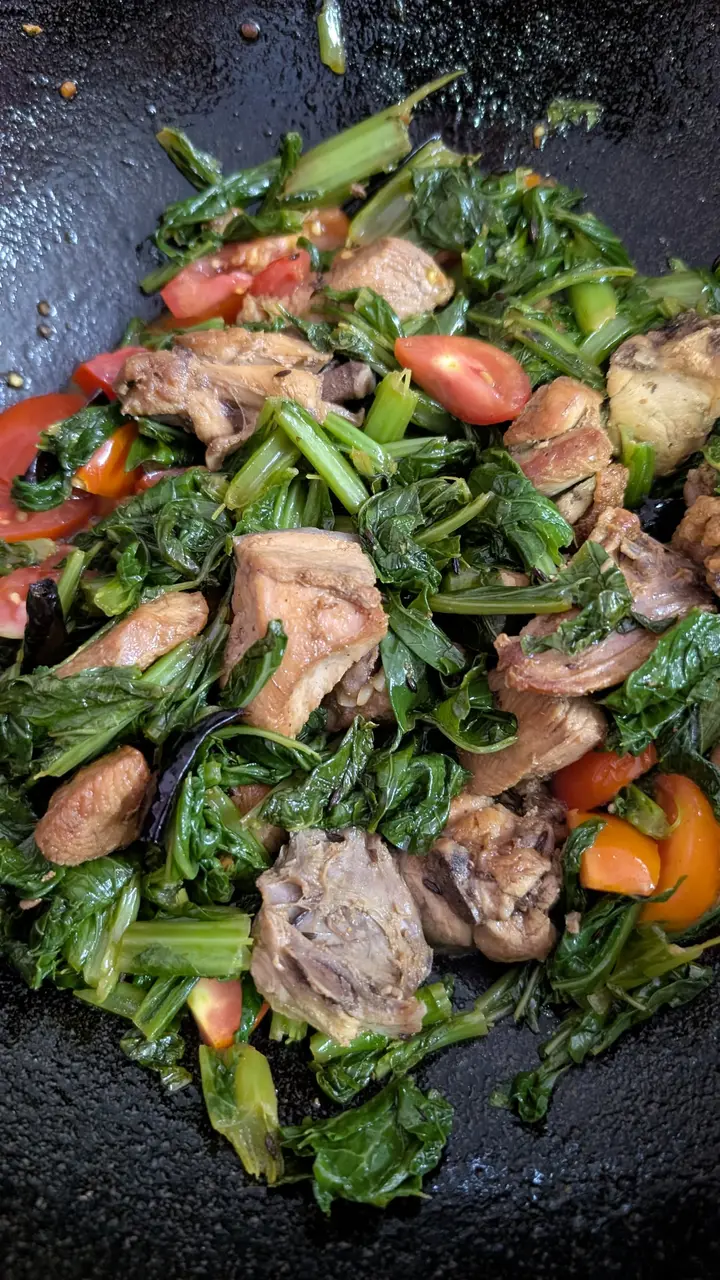Pieces of meat stir-fried with mustard greens and tomato in a black wok