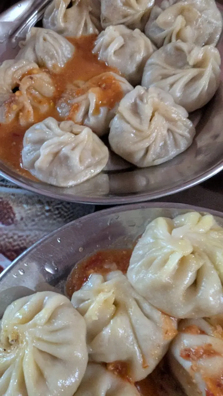 Two steel plates of steamed momos in tomato achar