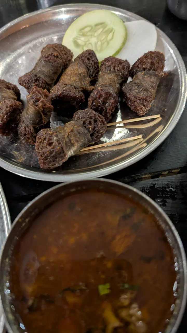 A steel plate of dark fried meat rolls with cucumber and radish slices, next to a bowl of meat curry