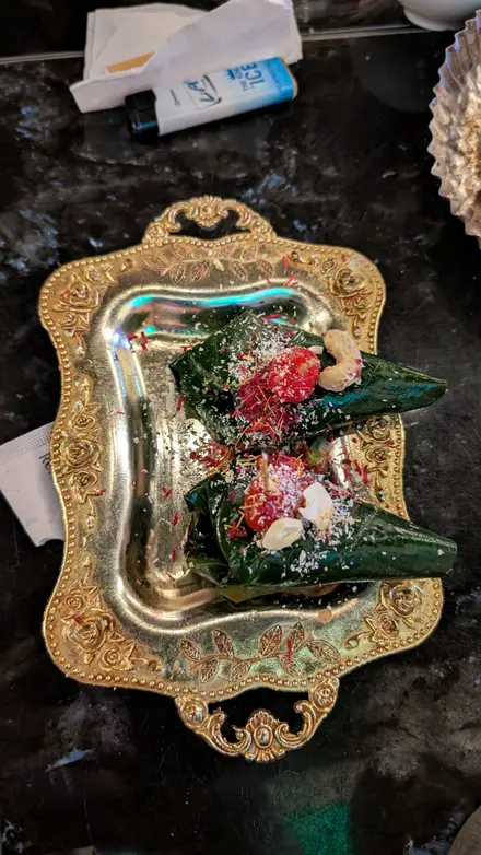 Two folded betel leaves topped with cherries, cashews and coloured coconut, on an ornate gold tray