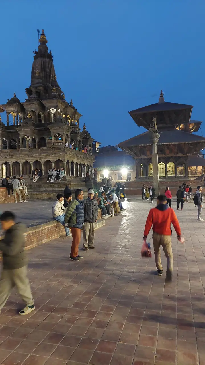 Patan Durbar Square at dusk: the stone Krishna Mandir and a pagoda temple against a deep blue sky, people strolling