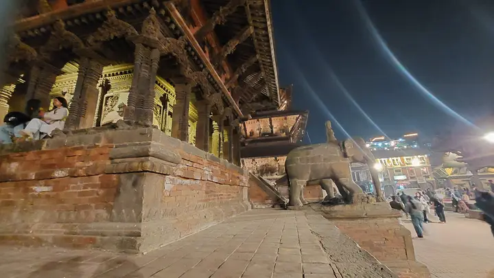 A carved wooden temple in Patan Durbar Square at night, with a stone elephant guarding its steps