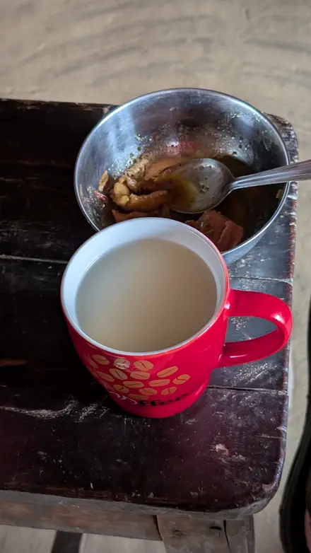 A red mug of milk tea on a worn wooden stool next to a steel bowl with the last pieces of meat curry