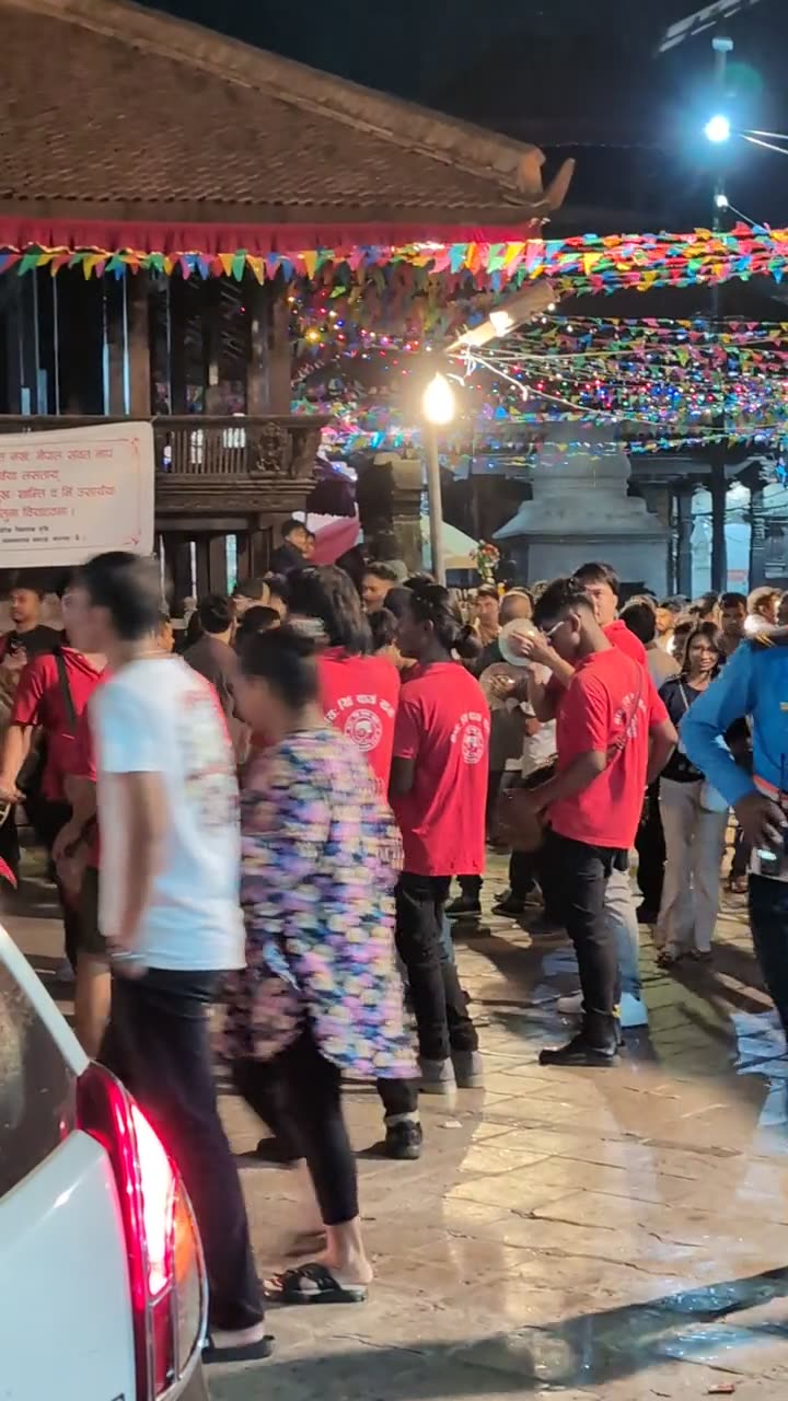 Crowds and a group in red T-shirts walking through Kathmandu Durbar Square at night under strings of lights