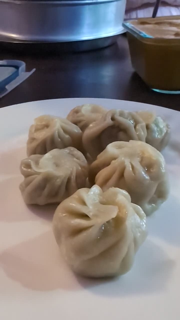 A plate of freshly steamed momos with a bowl of achar behind