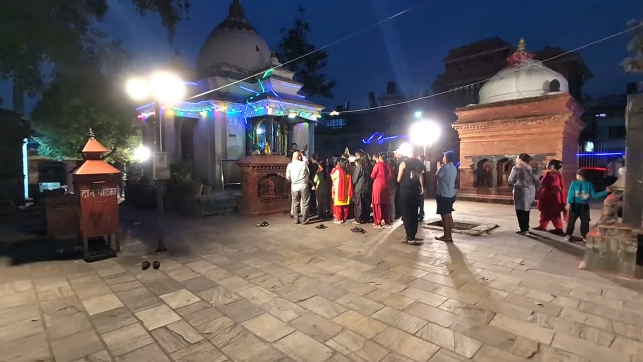 Worshippers queue at a lit, white-domed shrine in the evening