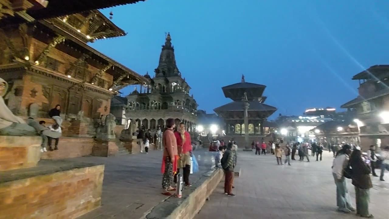 A slow pan across Patan Durbar Square at dusk, with temples, the palace and people walking