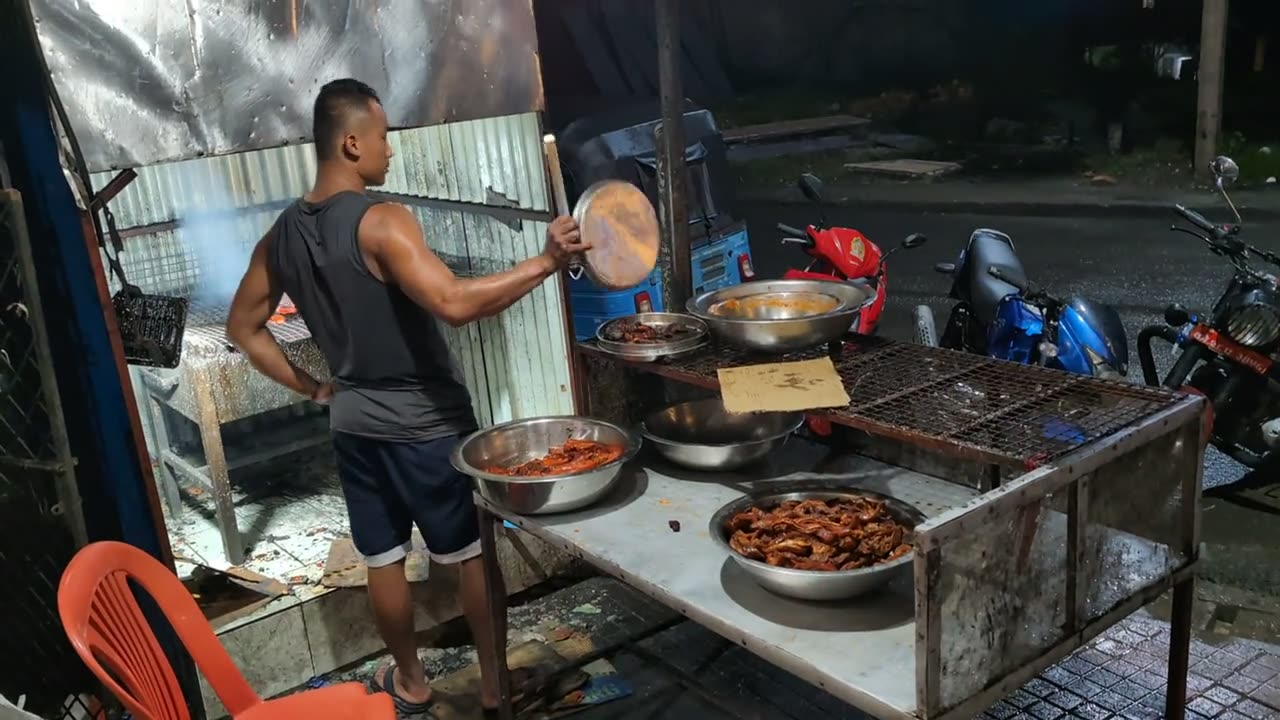 A man fans a charcoal grill of meat skewers at a roadside stall at night