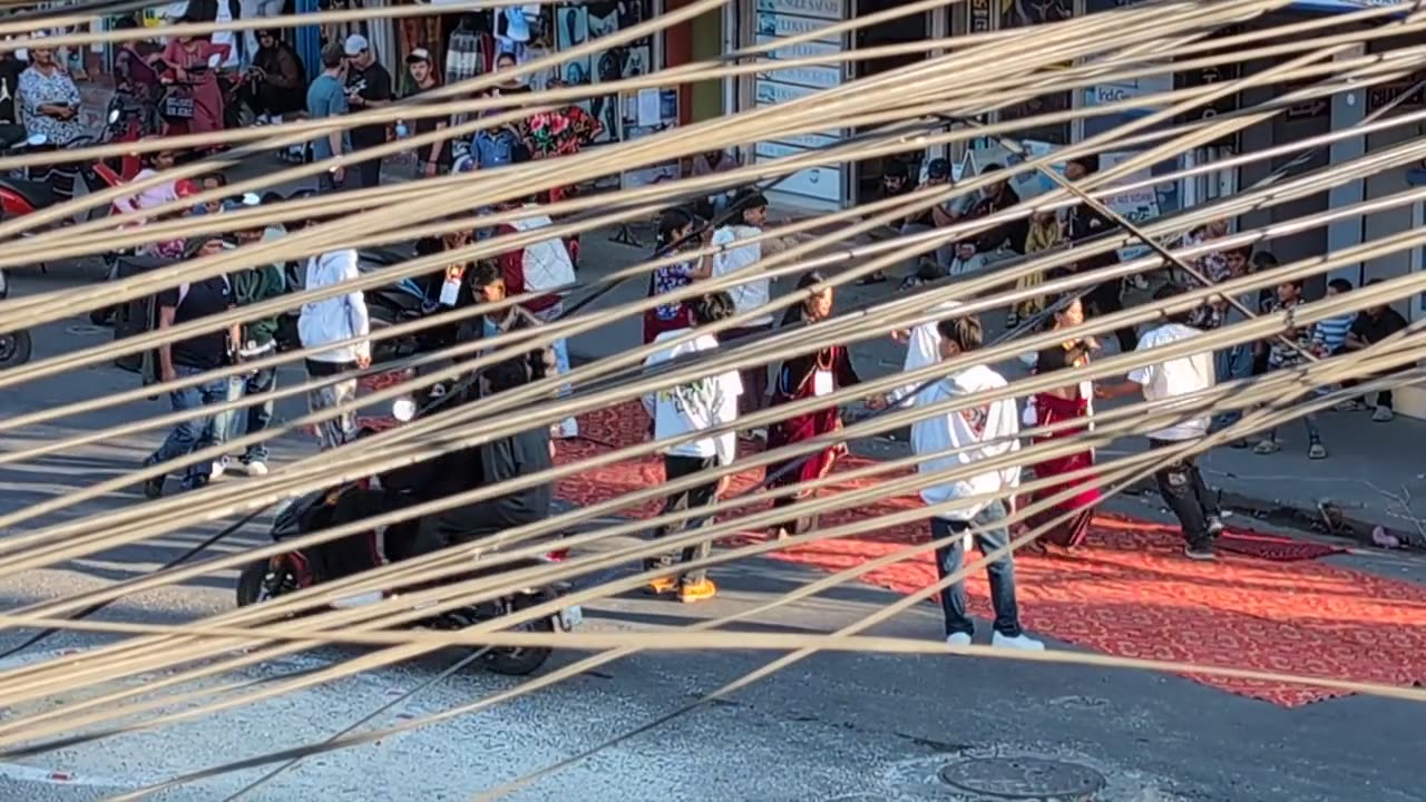 The same street dance seen from above, through a row of strings